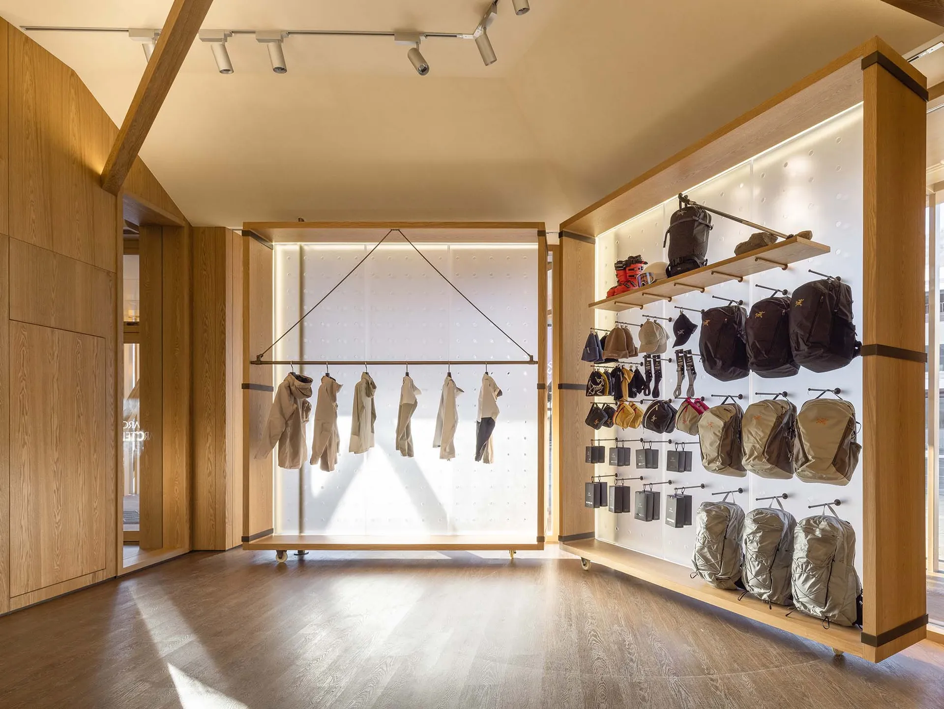 Modern retail store featuring a hanging display of garments on a white pegboard wall, with a variety of backpacks and accesso