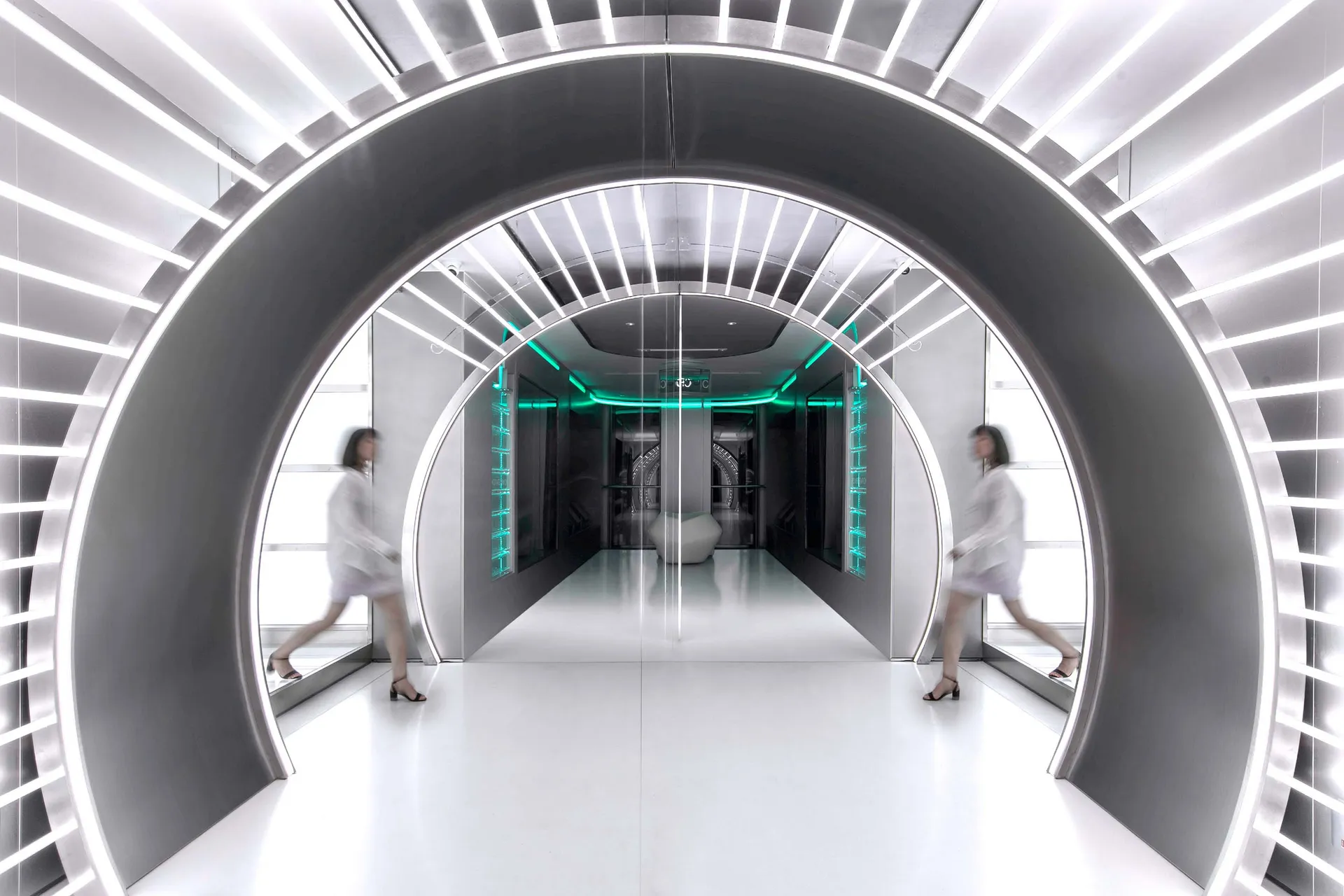 A modern hallway featuring a futuristic metal tunnel with bright lights and green accents, leading to a futuristic room with 
