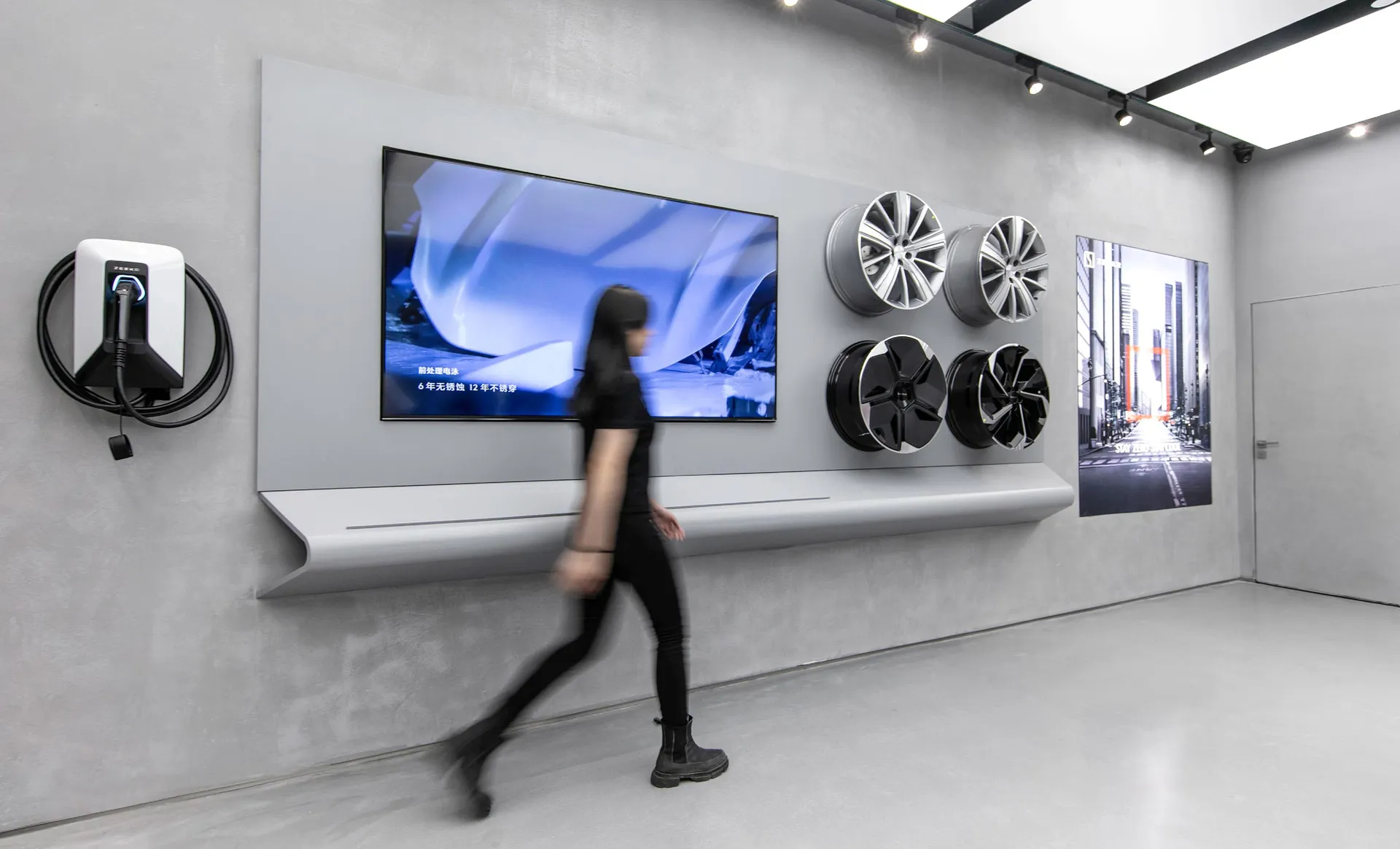 一位女士走過展示金屬輪圈與大型電視螢幕的現代室內空間。