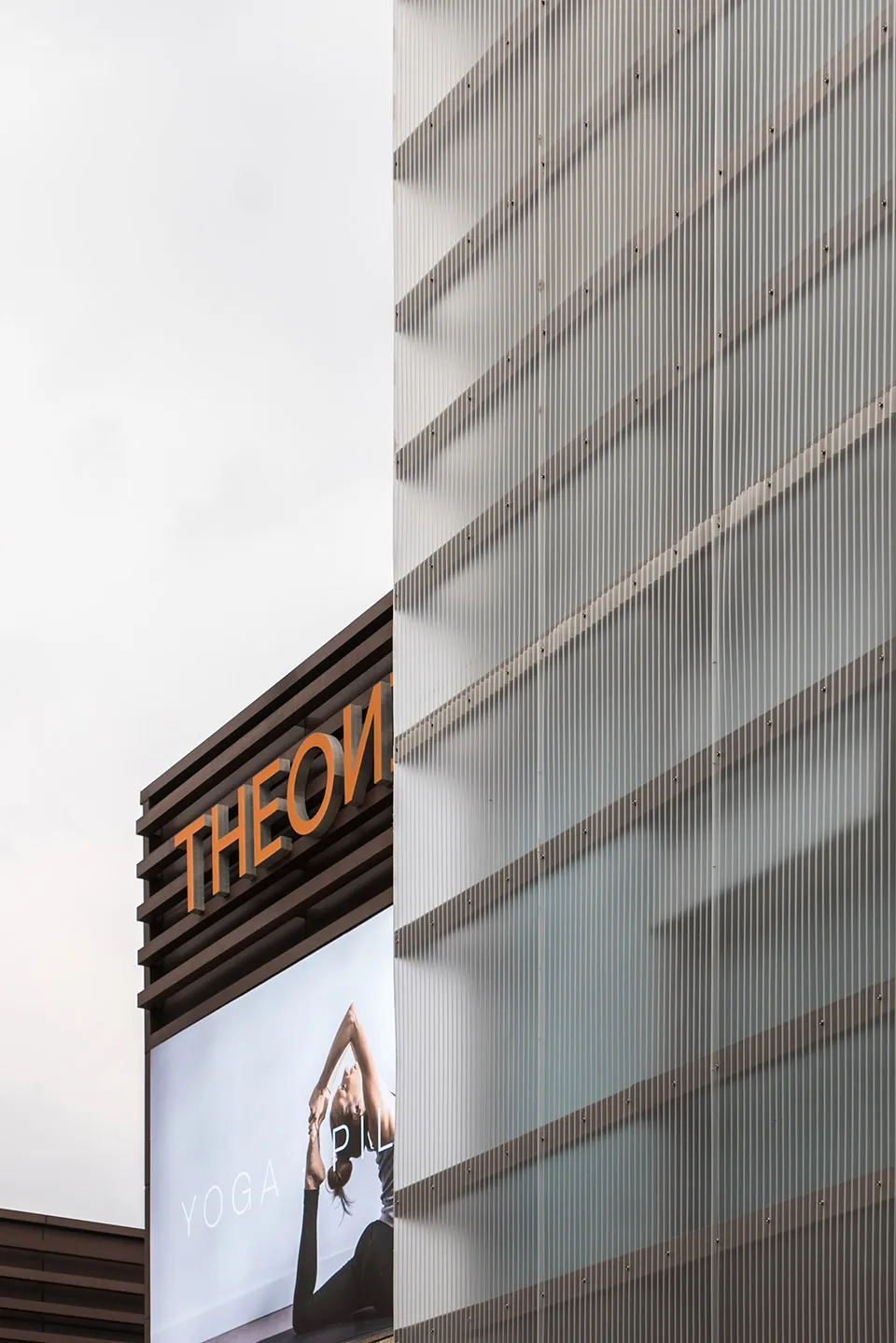 A modern commercial building with a glass façade and a sign that reads 'THEON YOGA PILATES'.