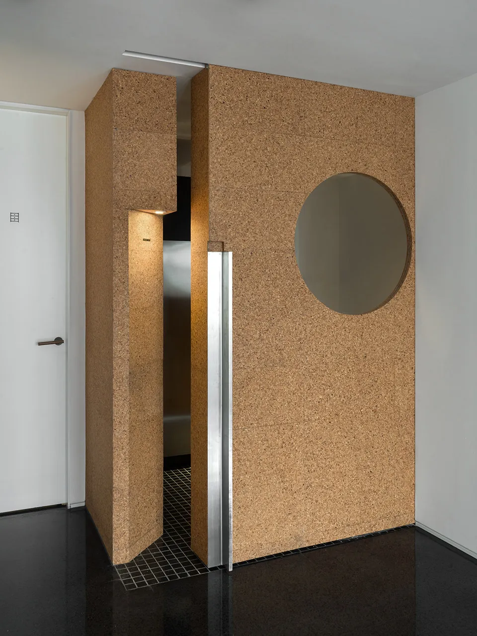 A modern entryway featuring cork panels with a circular mirror and a light fixture