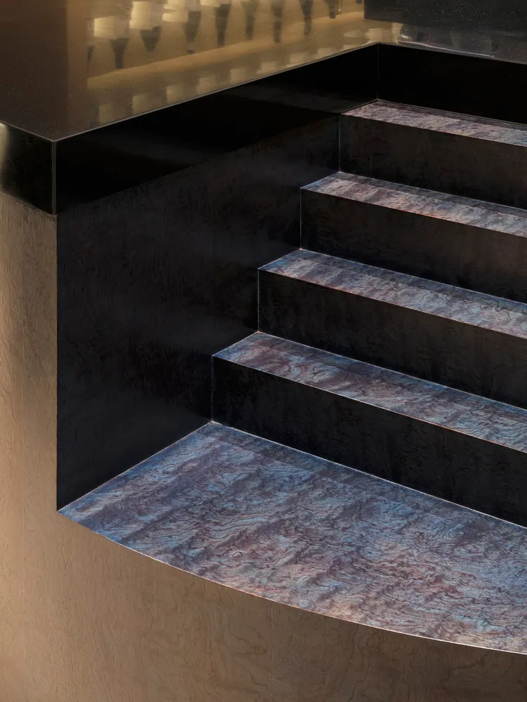 A metallic staircase with marble steps and a black metallic wall.