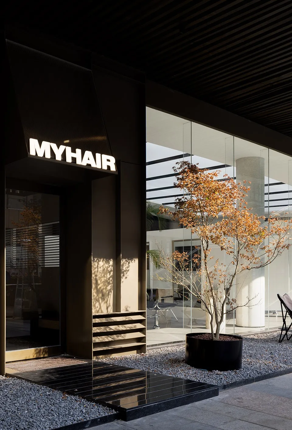 A modern hair salon entry featuring a glass and concrete façade.