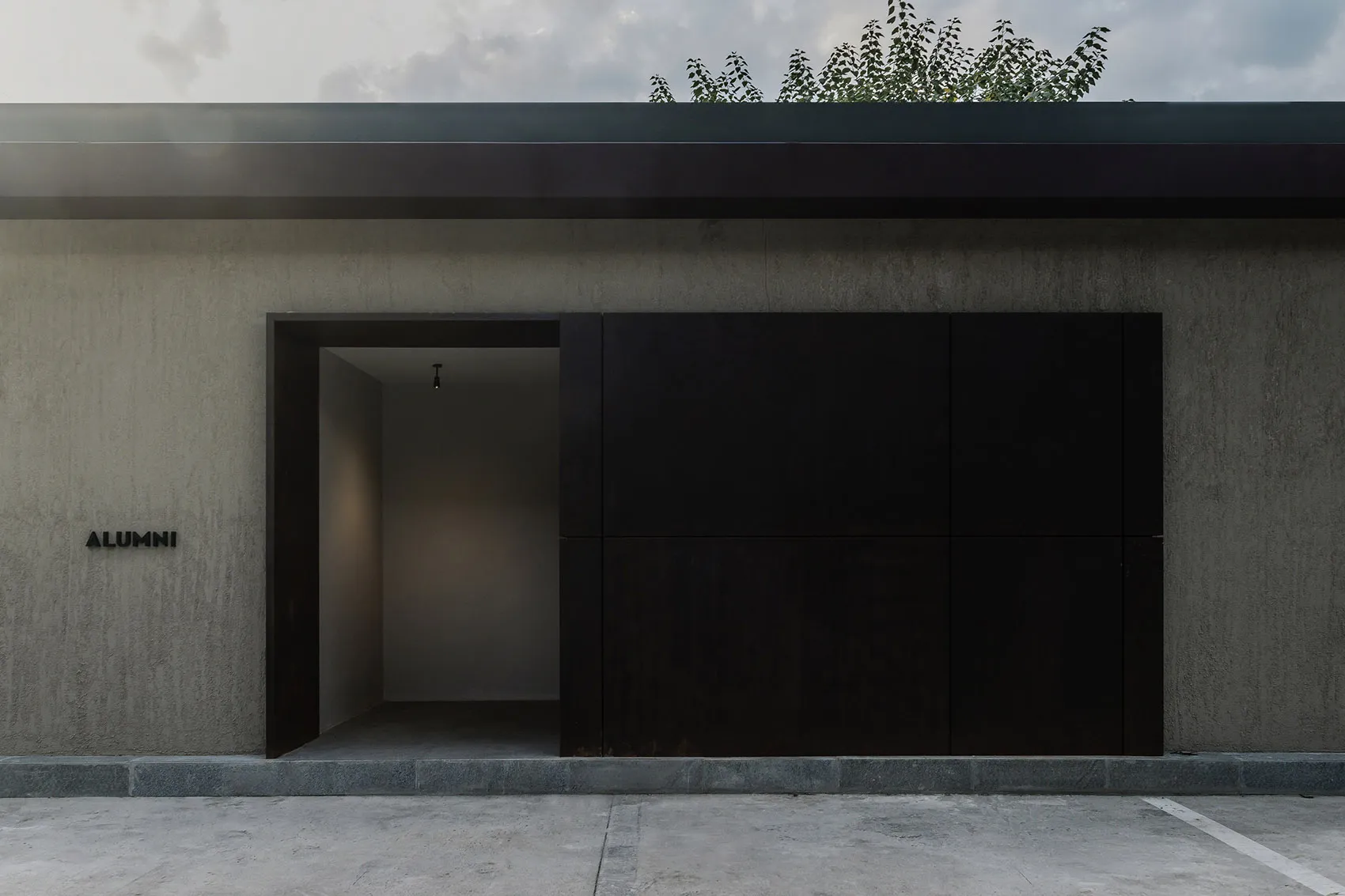 Minimalist building exterior with black metal panels and a concrete base, viewed from the parking garage.