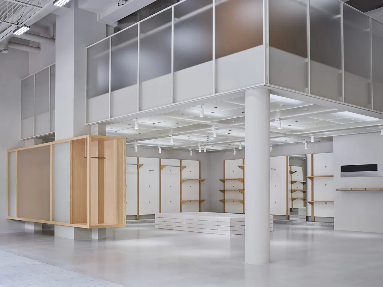 A minimalist retail store featuring white walls, concrete flooring, and wooden shelves.