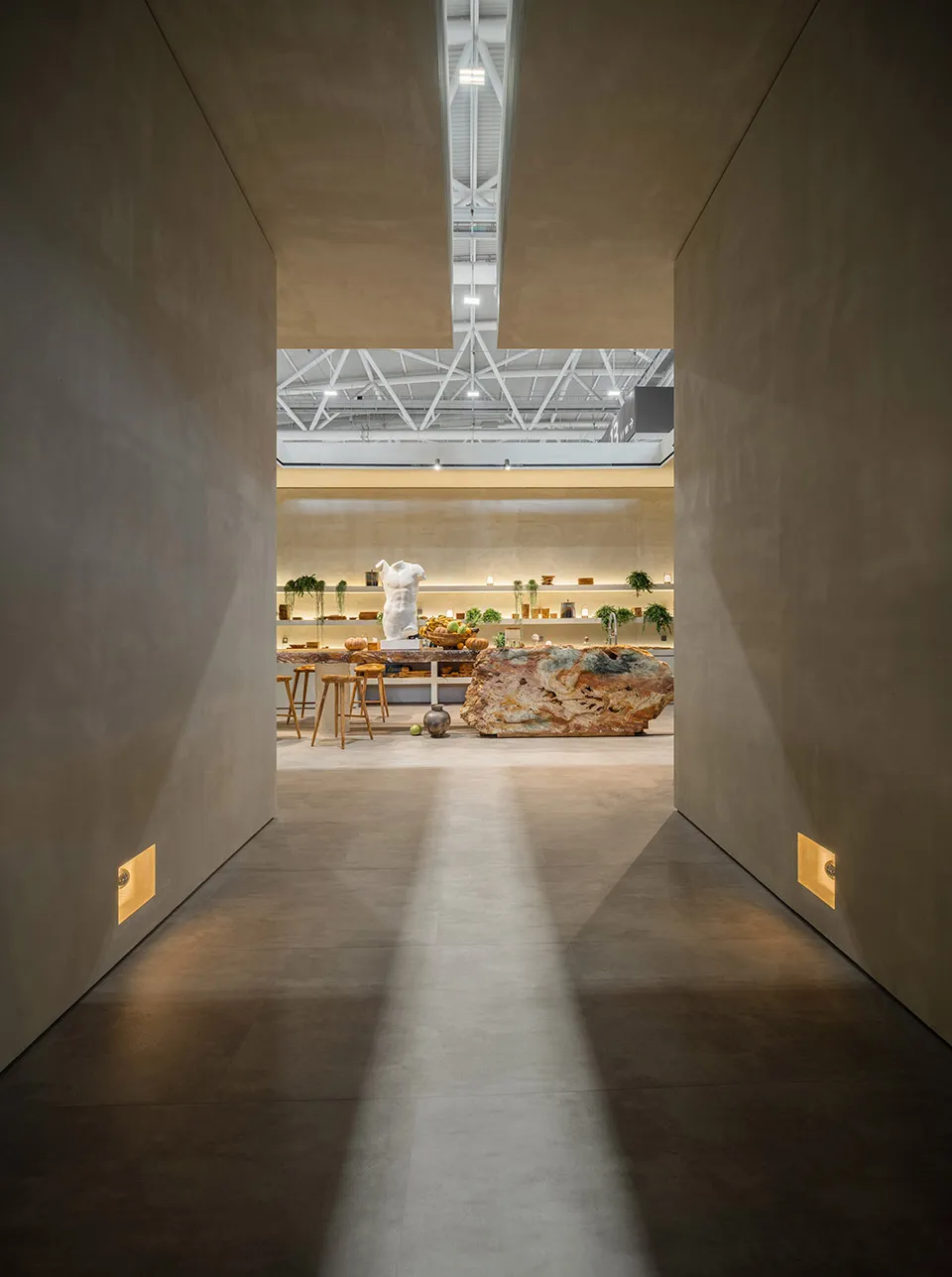 A minimalist commercial space featuring a concrete floor and walls, industrial-style lighting, and a central piece of furnitu