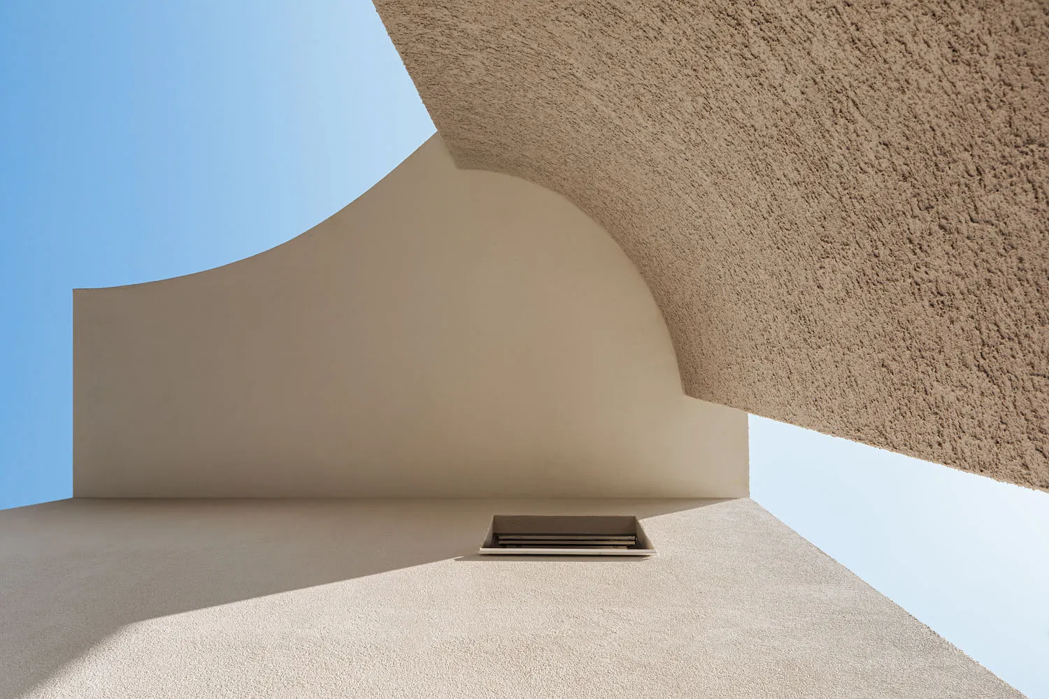 A modern building with a textured concrete exterior against a clear blue sky.