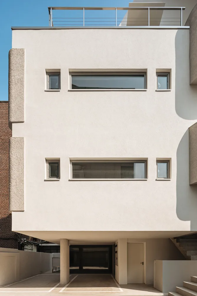 A modern building with a concrete exterior featuring large windows and a rooftop balcony.