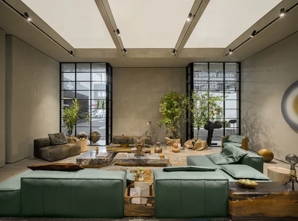 A modern, minimalist living room with concrete walls, furniture, and lighting, featuring green sofas and decorative plants.