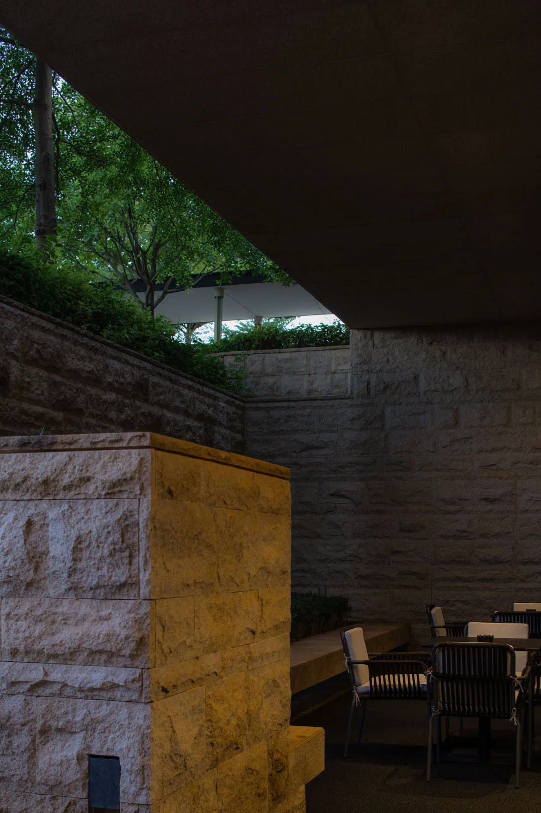 Modern outdoor seating area with stone walls and greenery in the background.