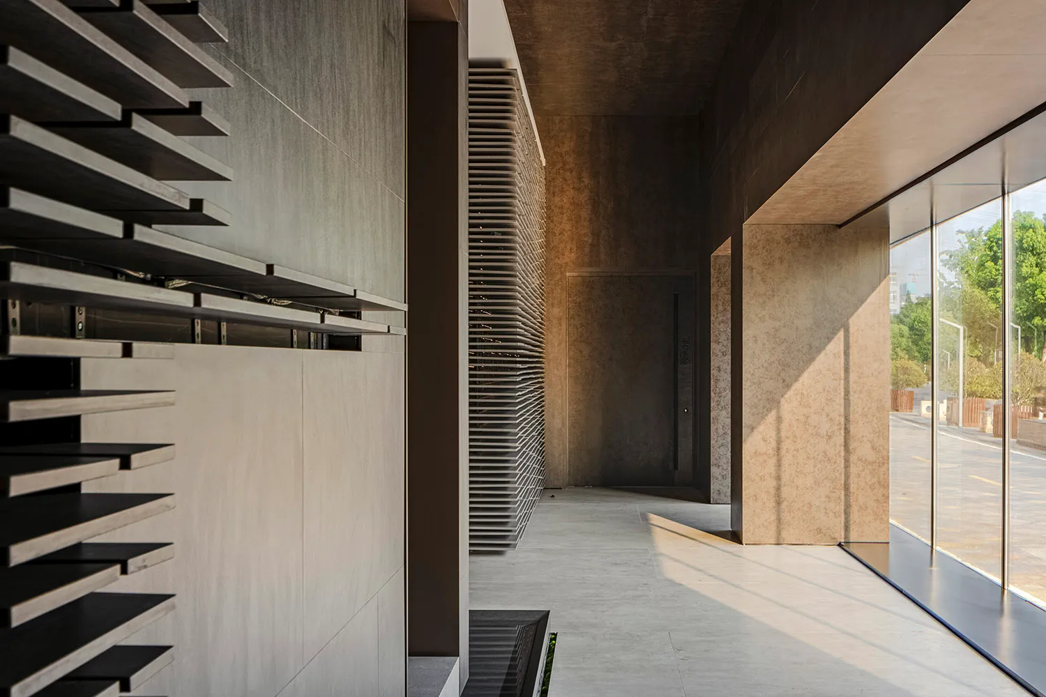 Modern, minimalist corridor with concrete walls, slatted feature wall, and large windows overlooking greenery.