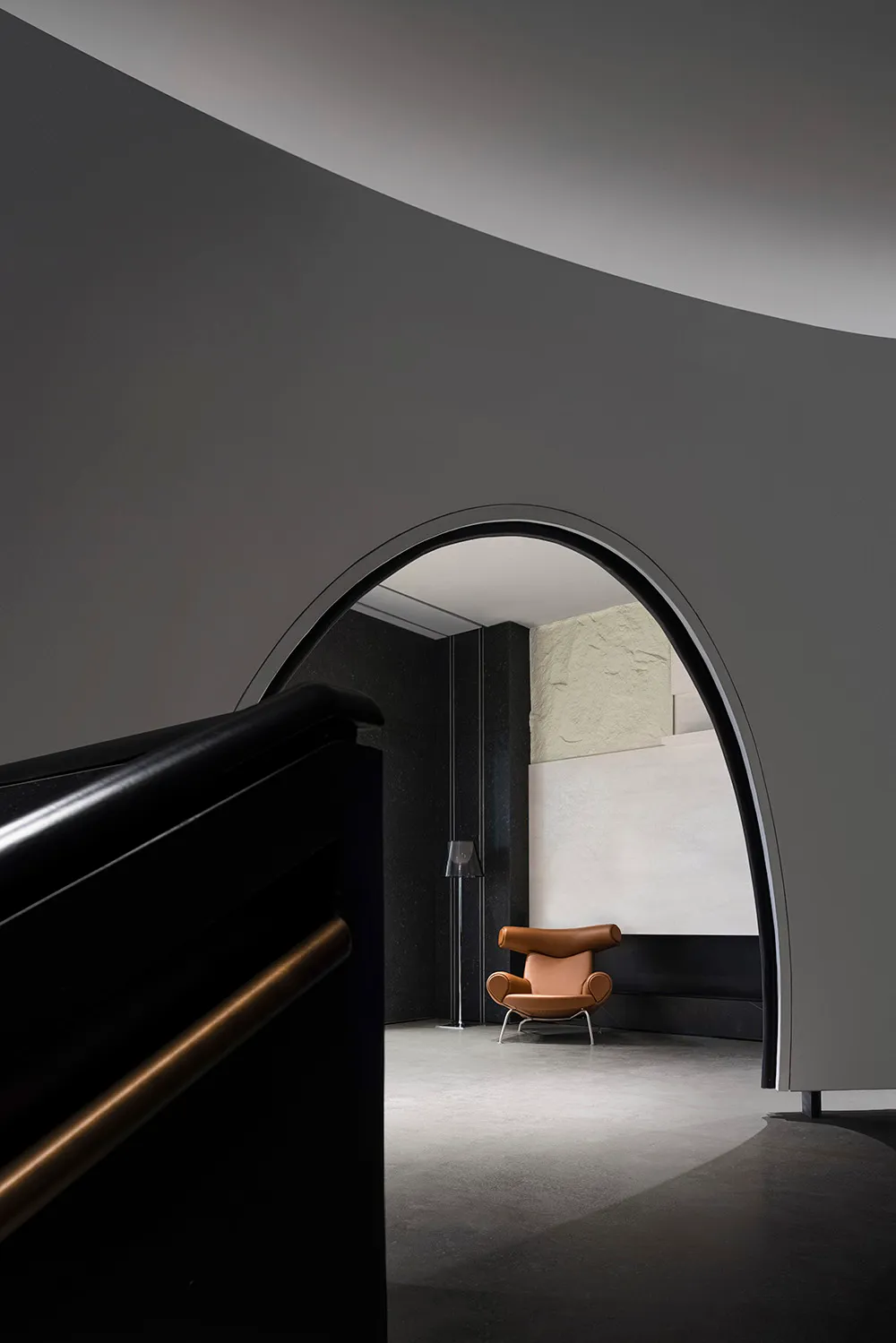 A minimalist interior design featuring dark concrete walls with an arched doorway leading to a lounge area with a single mode