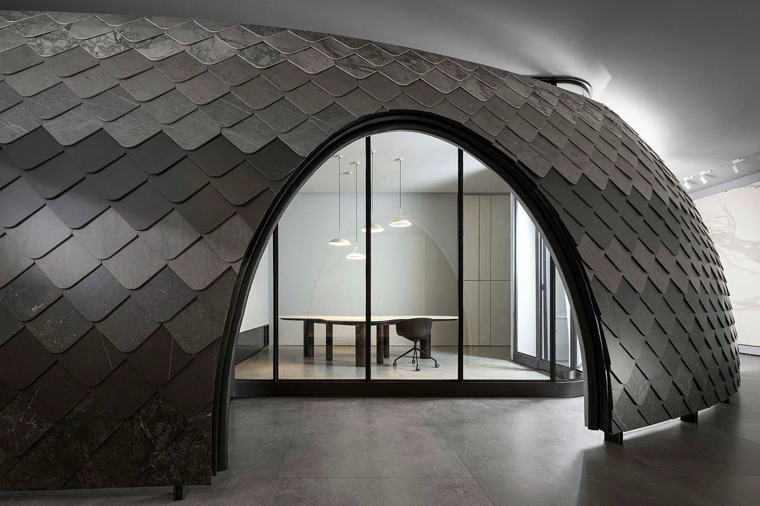 Modern office interior featuring metallic scalloped wall with arched doorway leading to a conference room with sleek design