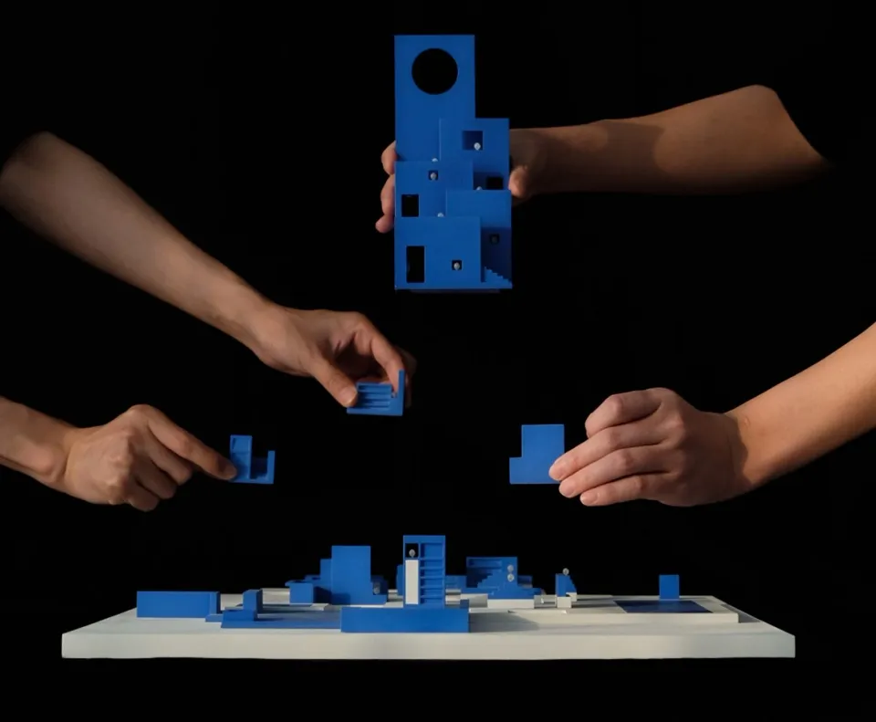 Four hands arranging a blue architectural model on a black background.