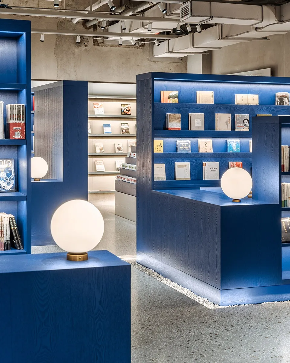 A modern bookstore interior designed with blue wooden shelves and spherical lights.