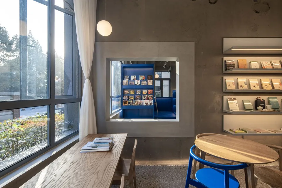 Modern minimalist restaurant interior with a window view featuring wood tables and blue chairs.
