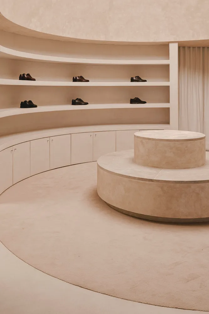 A minimalist retail space featuring concrete shelving and neatly arranged black leather shoes.