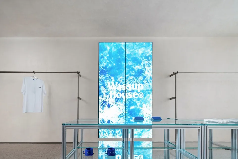 A minimalist retail storefront featuring a glass display case with a blue ocean-themed logo on a digital screen.
