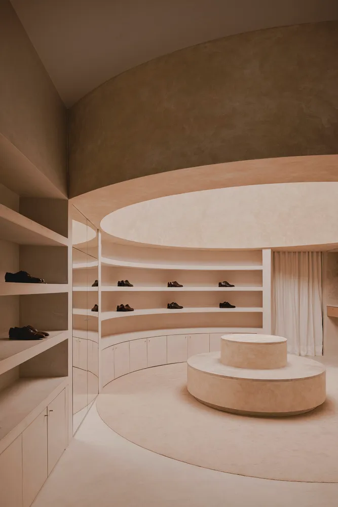 A minimalist display featuring shoes on concrete shelves and a concrete pedestal.