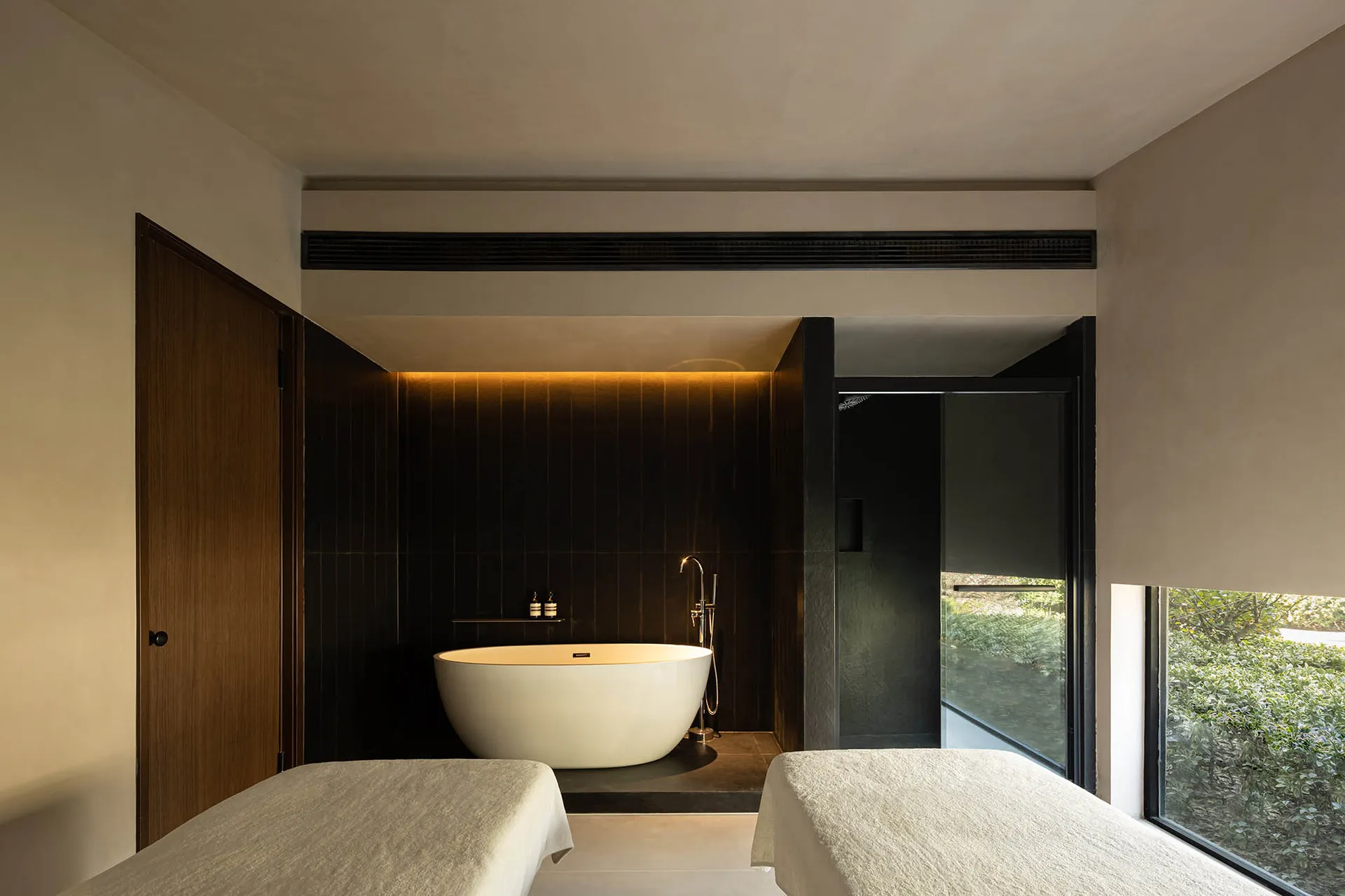Minimalist spa room with a freestanding bathtub, massage beds, and glass walls