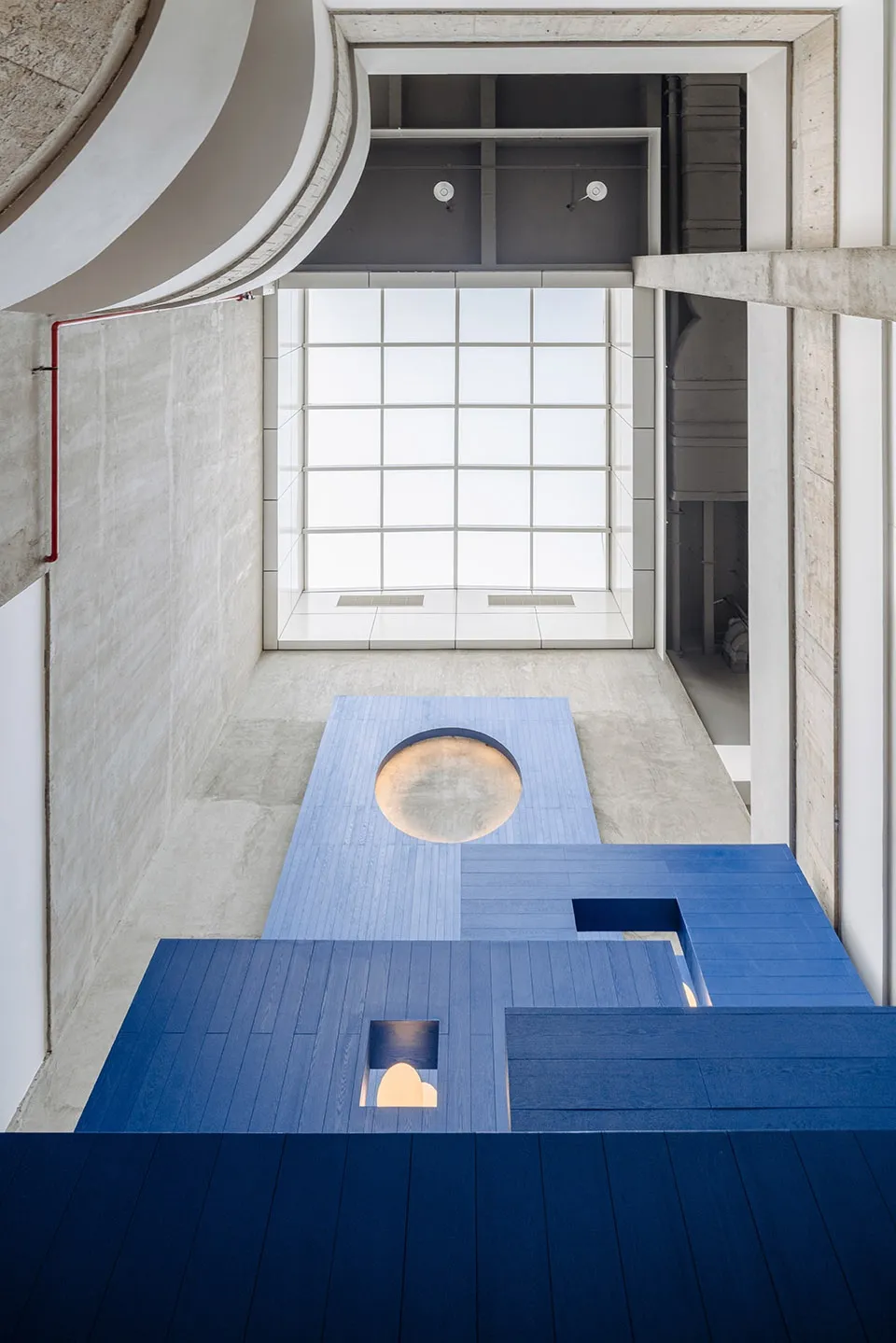 Modern interior space with concrete flooring and a circular opening, illuminated by warm lighting.