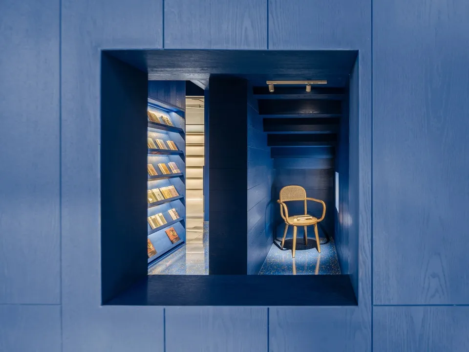 A minimalist library interior with blue walls, wooden shelves, and a wooden chair.