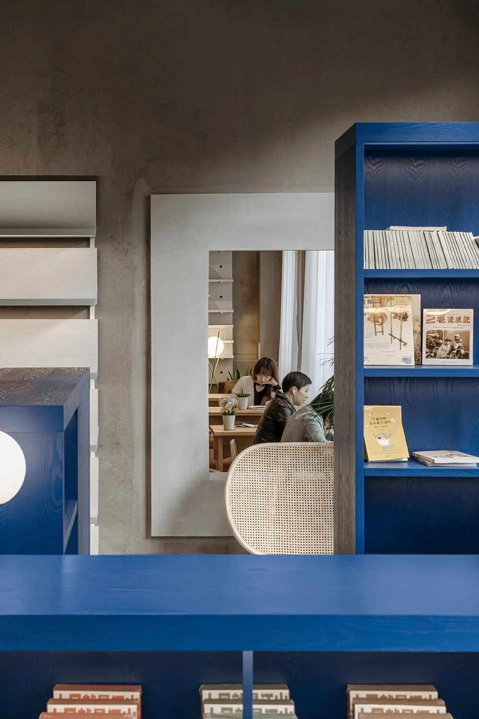 A modern library interior featuring blue wooden shelves with books and a woven chair.