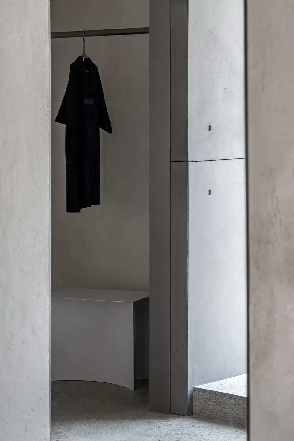 A minimalist wardrobe space featuring concrete elements and a single black garment hanging on a rod.