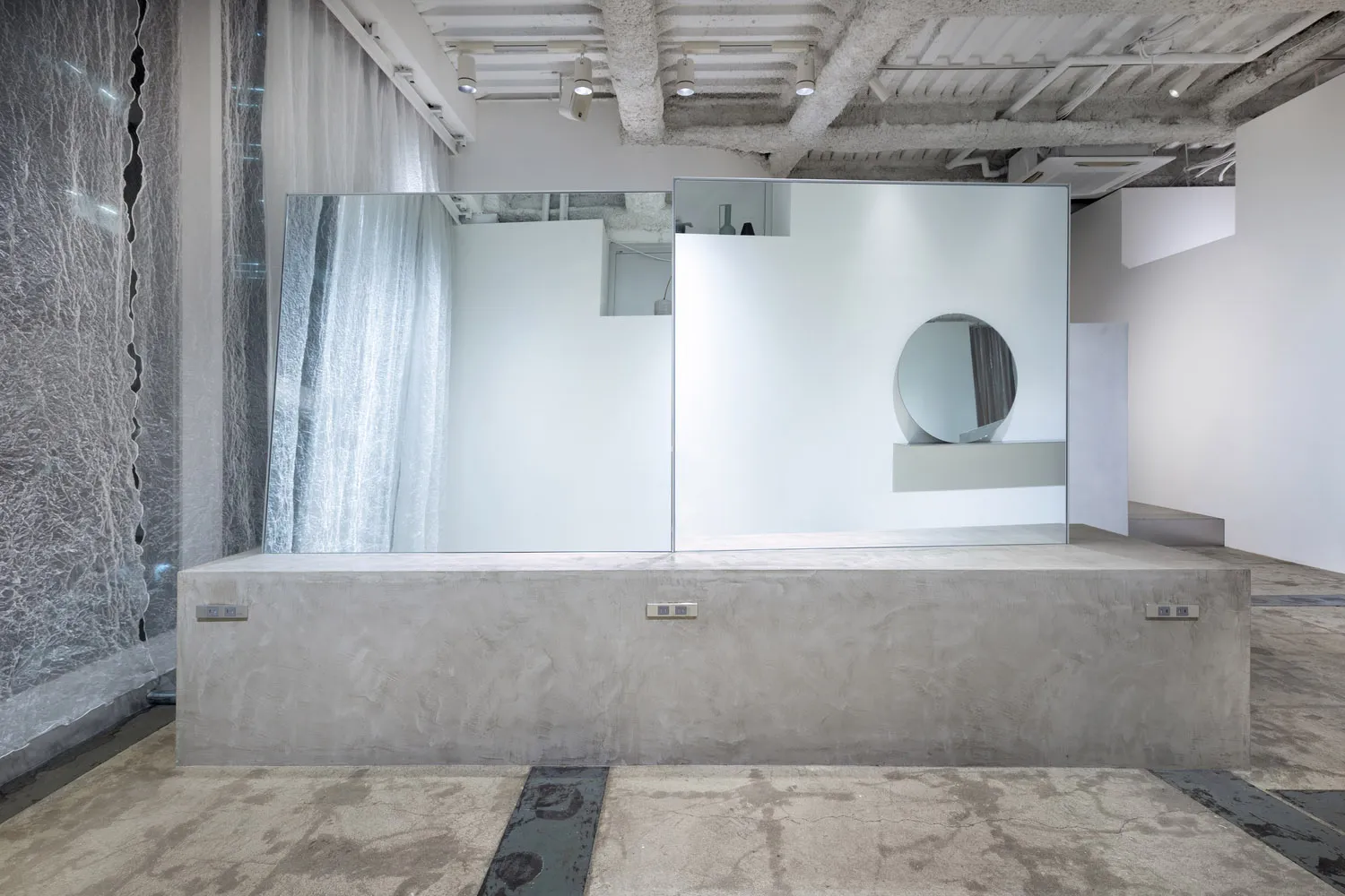 An abstract, minimalist installation featuring large sheets of frosted glass mounted on a concrete pedestal.