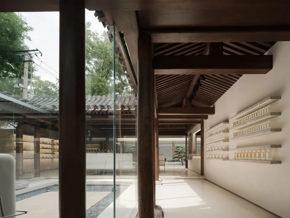 A modern gallery space featuring glass walls and wooden beams.