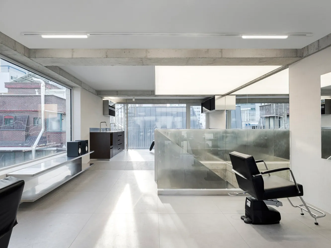 Modern industrial-style barber shop interior with concrete, glass, and metal elements.