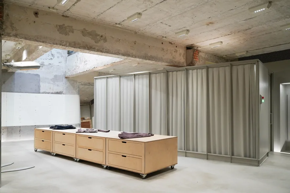 Modern interior space featuring concrete walls, wooden cabinets, and clothing displayed on a table.