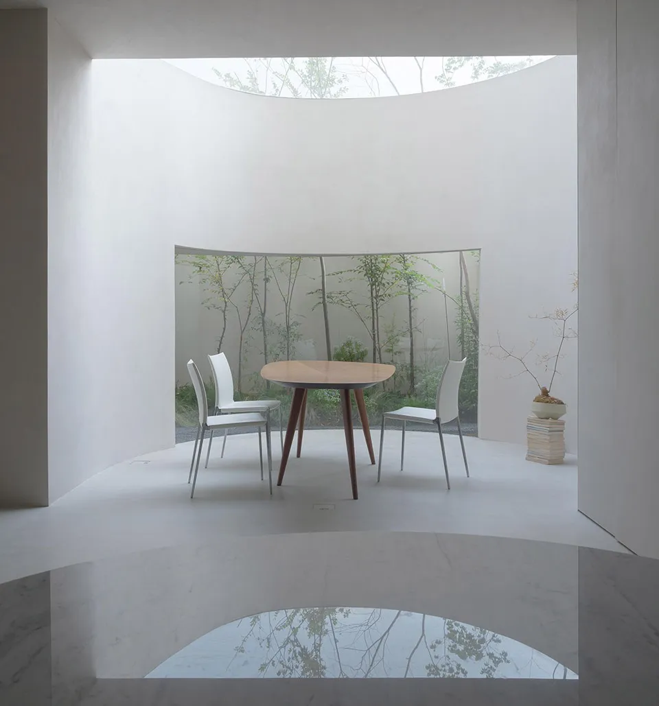 A minimalist interior space with a white table and chairs surrounded by greenery.