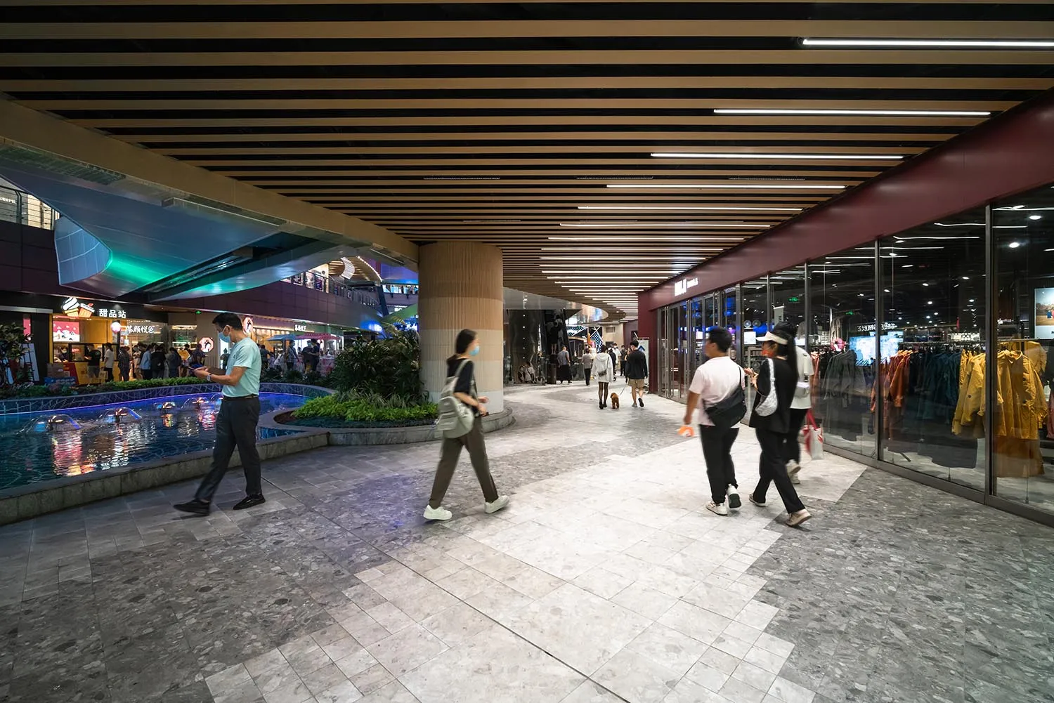 People walking in a modern shopping mall featuring concrete, glass, and tile flooring.