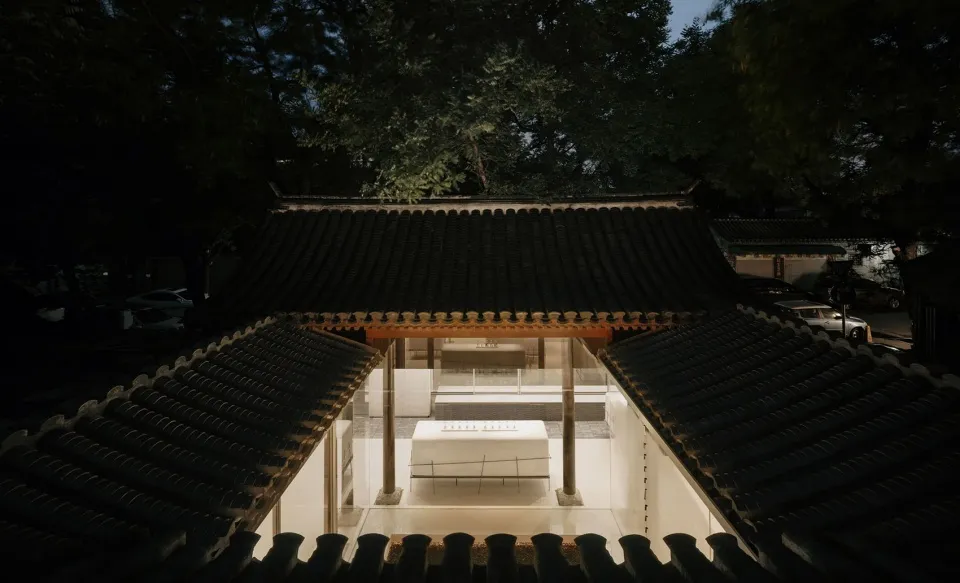 A traditional Japanese teahouse with black tiled roofs and white walls illuminated by lights at dusk.
