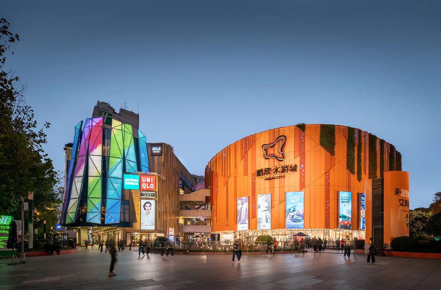 A modern shopping mall with a multicolor metal-clad exterior and illuminated signage.