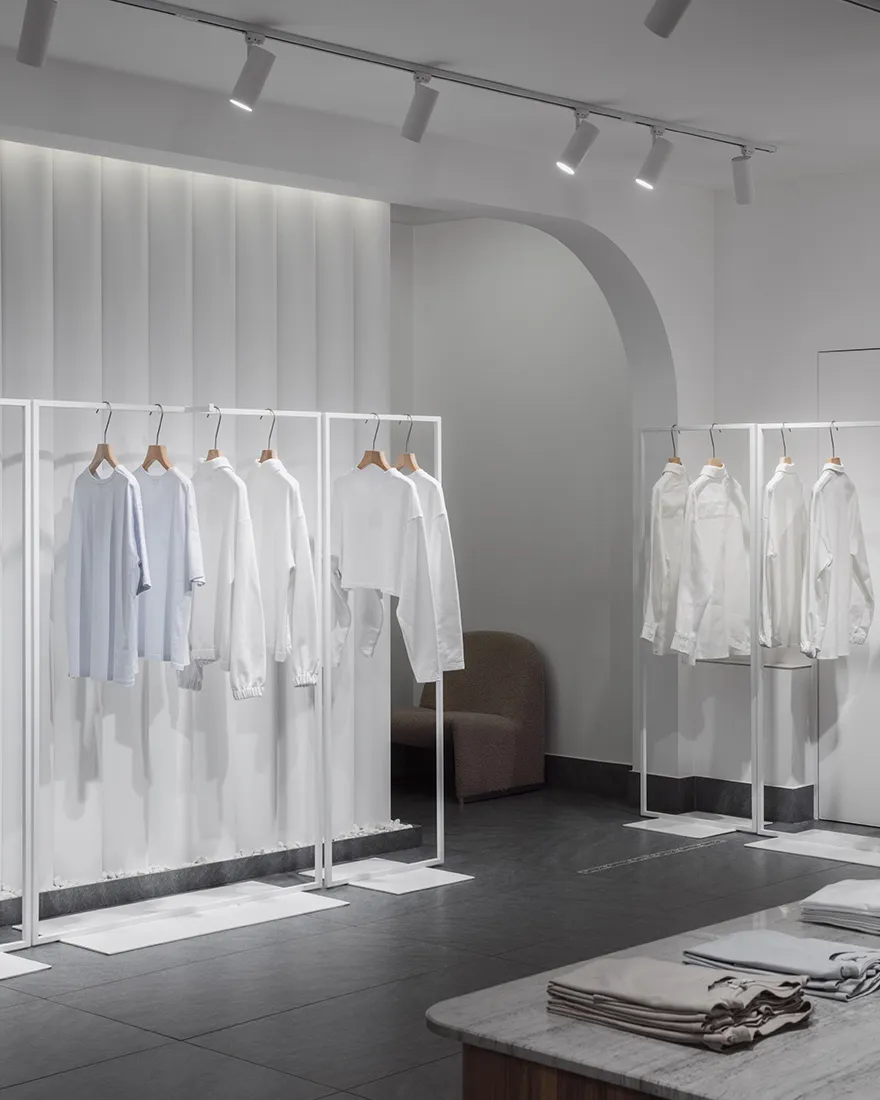 A minimalist fashion shop featuring white clothes on metallic frames and a clean, modern aesthetic
