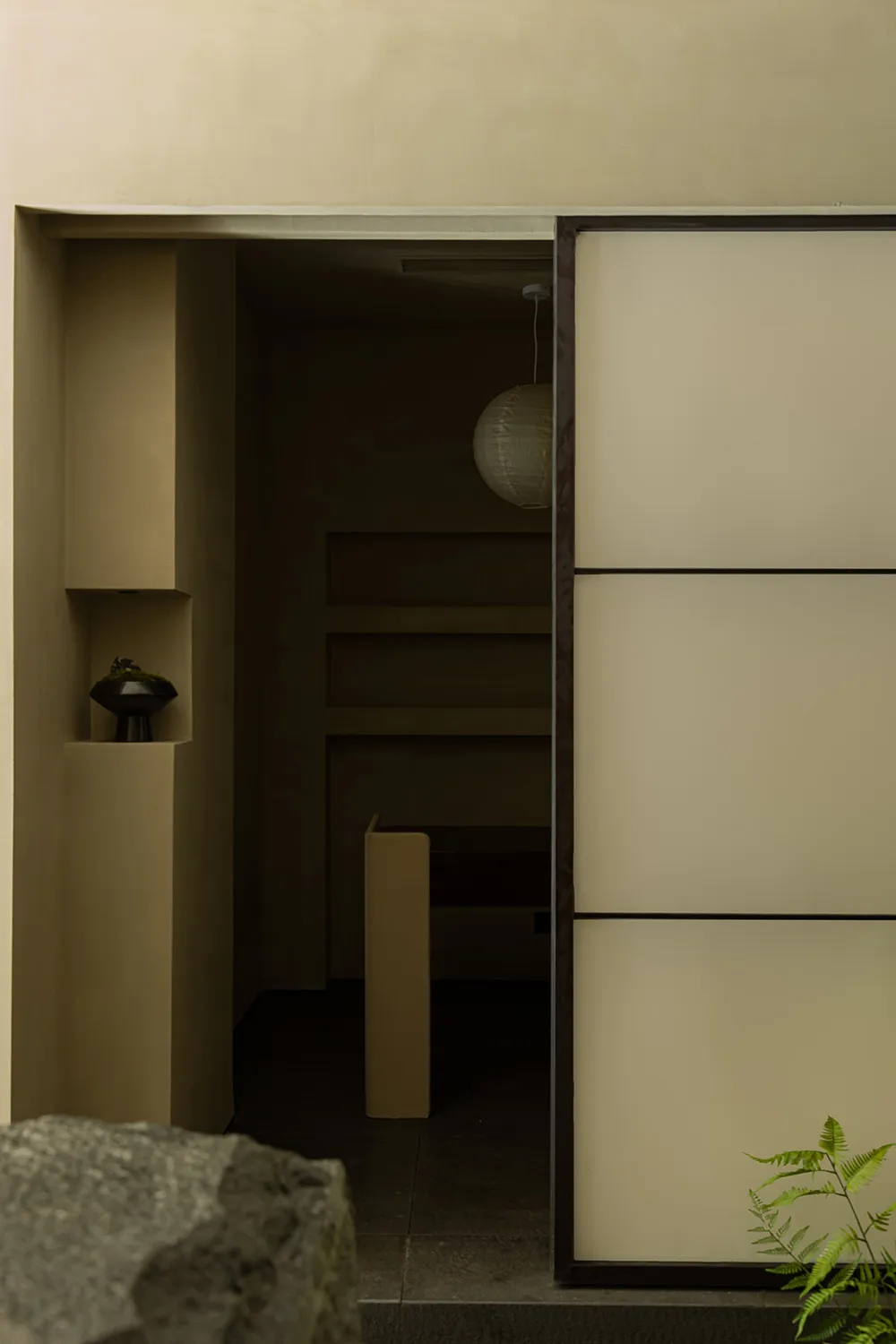 A minimalist entrance space with a door, shelves, and a hanging light fixture.