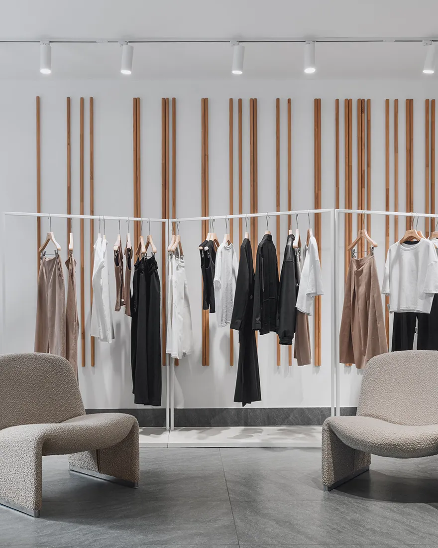 A minimalist clothing store interior with white racks, metallic rails, and wooden backdrop.