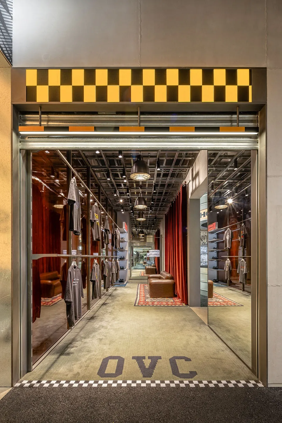 An industrial-style clothing store interior with concrete flooring and walls, featuring clothes displayed on racks.