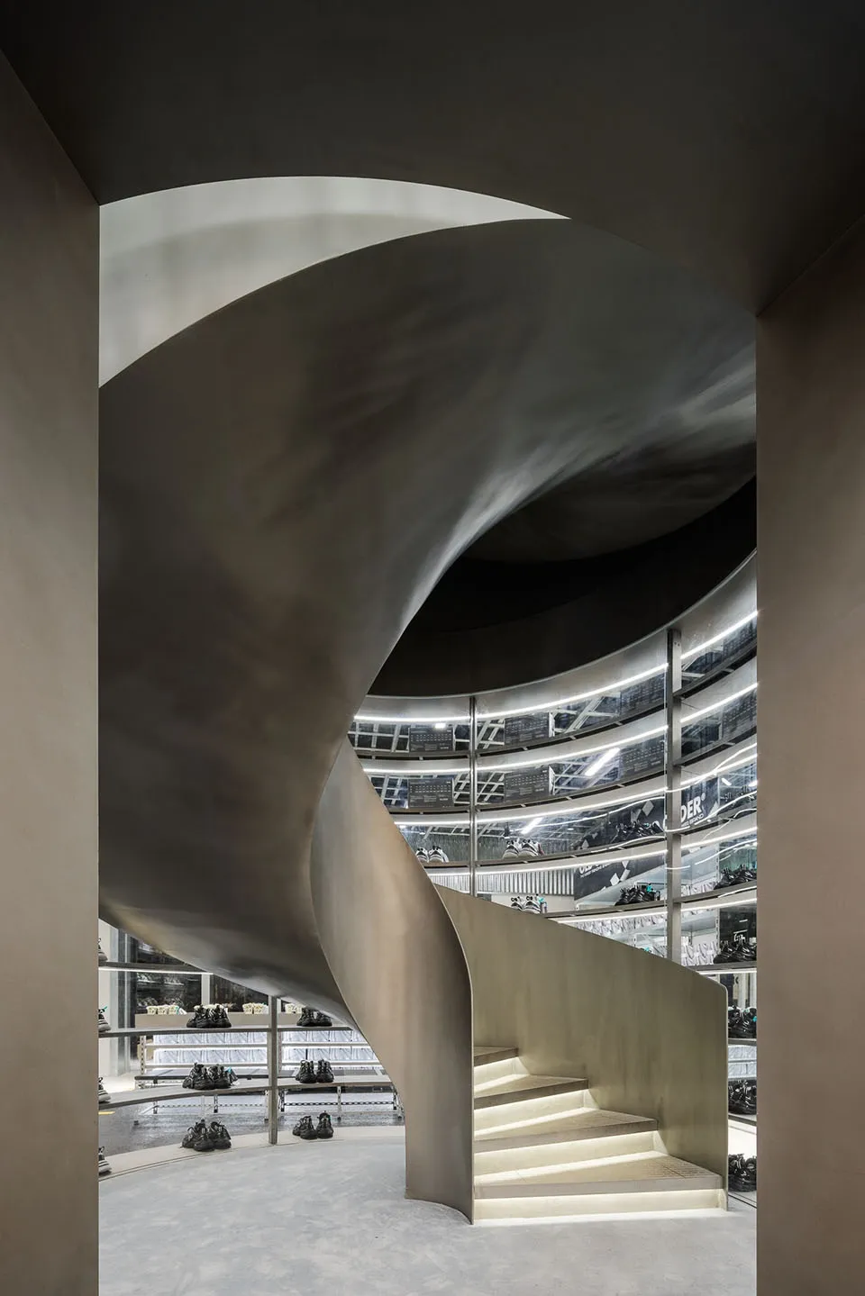 Modern architectural design featuring a spiraling staircase made of metal and glass, with a concrete ground level.