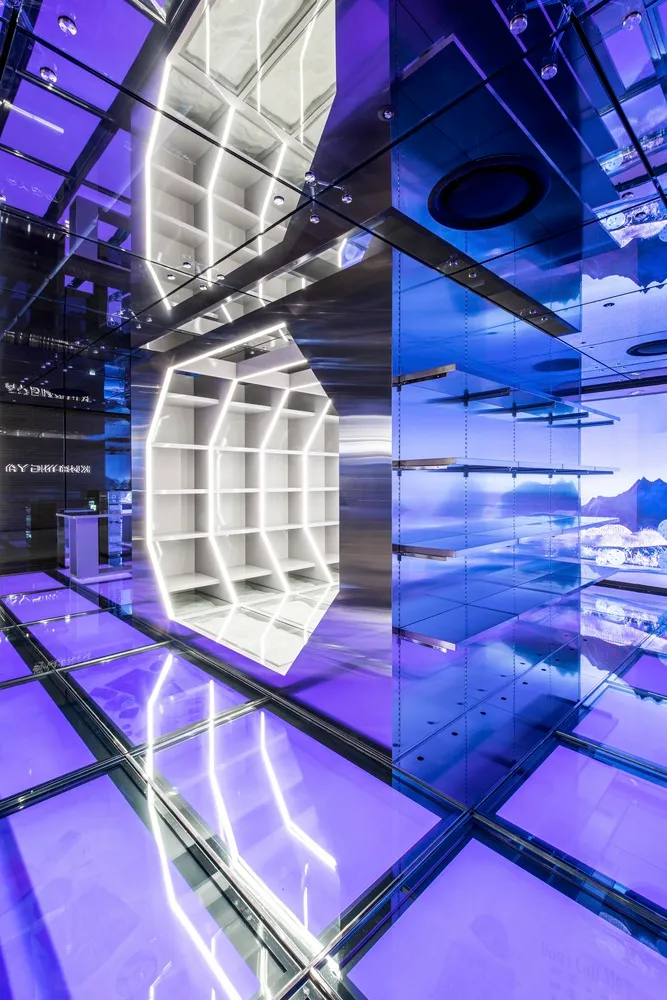 Modern minimalist exhibition space featuring glass walls, metallic structures, and ambient lighting.