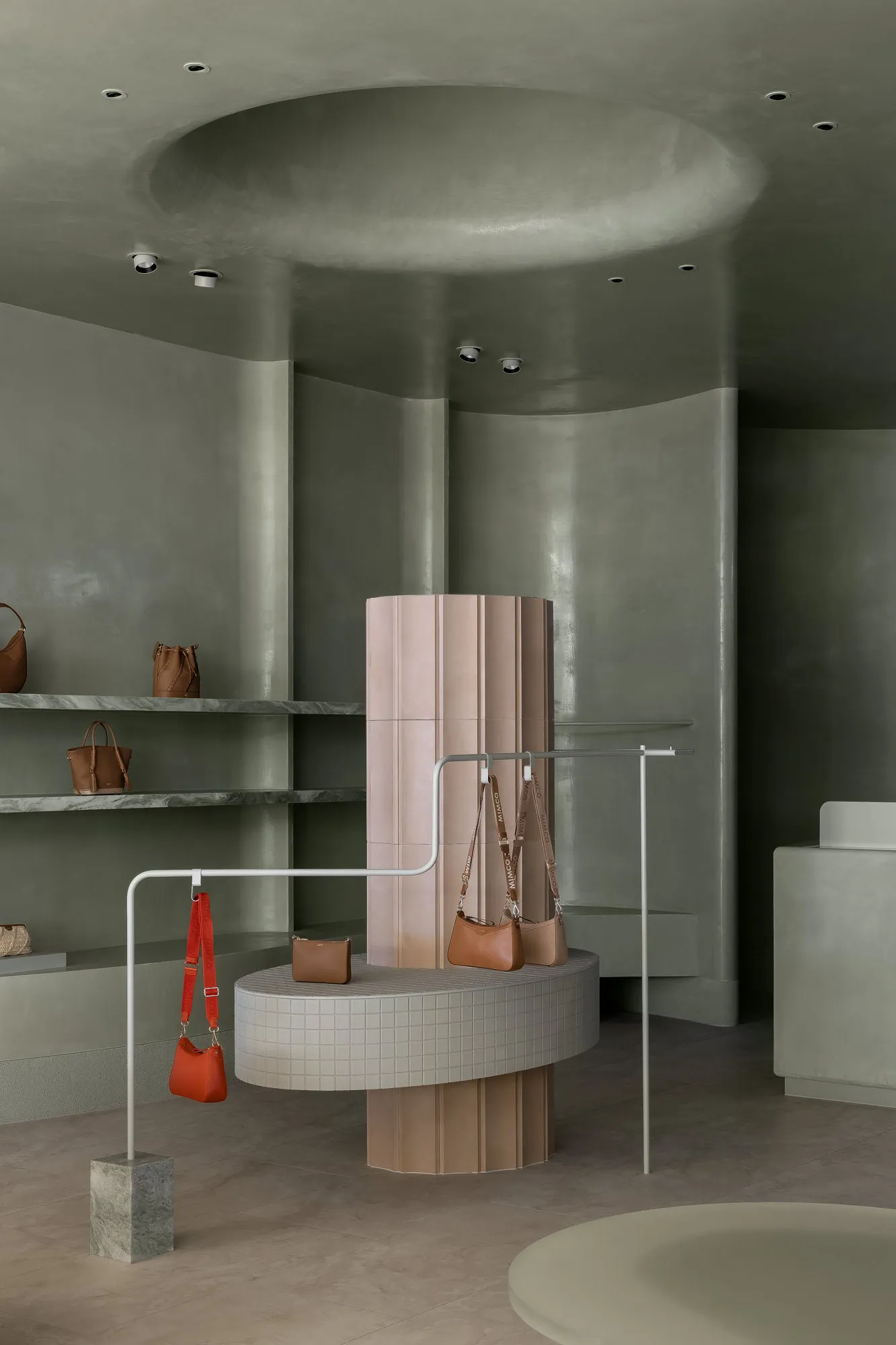 A minimalist retail space features concrete walls and flooring, with bags displayed on a cylindrical pedestal.
