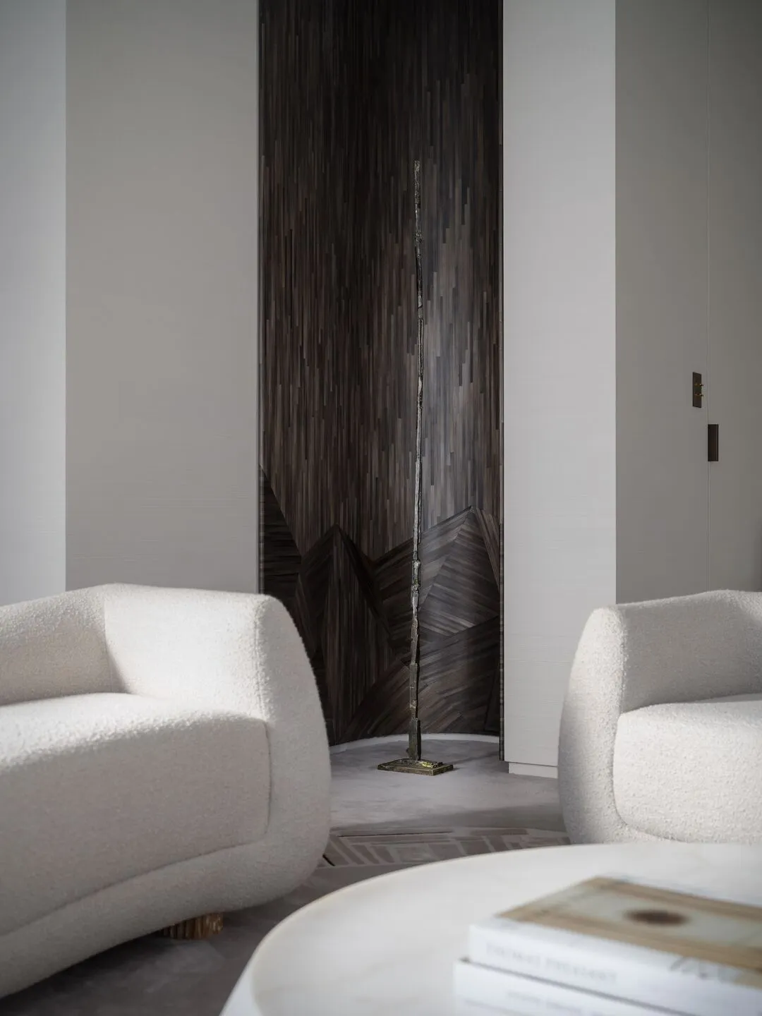 Modern minimalist living room with cream-colored fabric armchairs, marble center table, and abstract sculpture in the backgro
