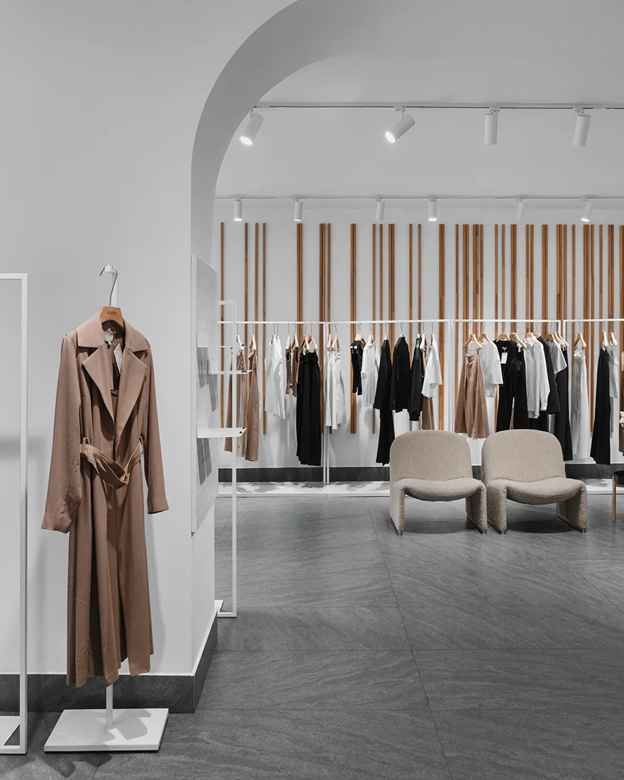 A modern retail store interior with minimalist design, featuring a coat hanging on a white display stand and clothing racks w