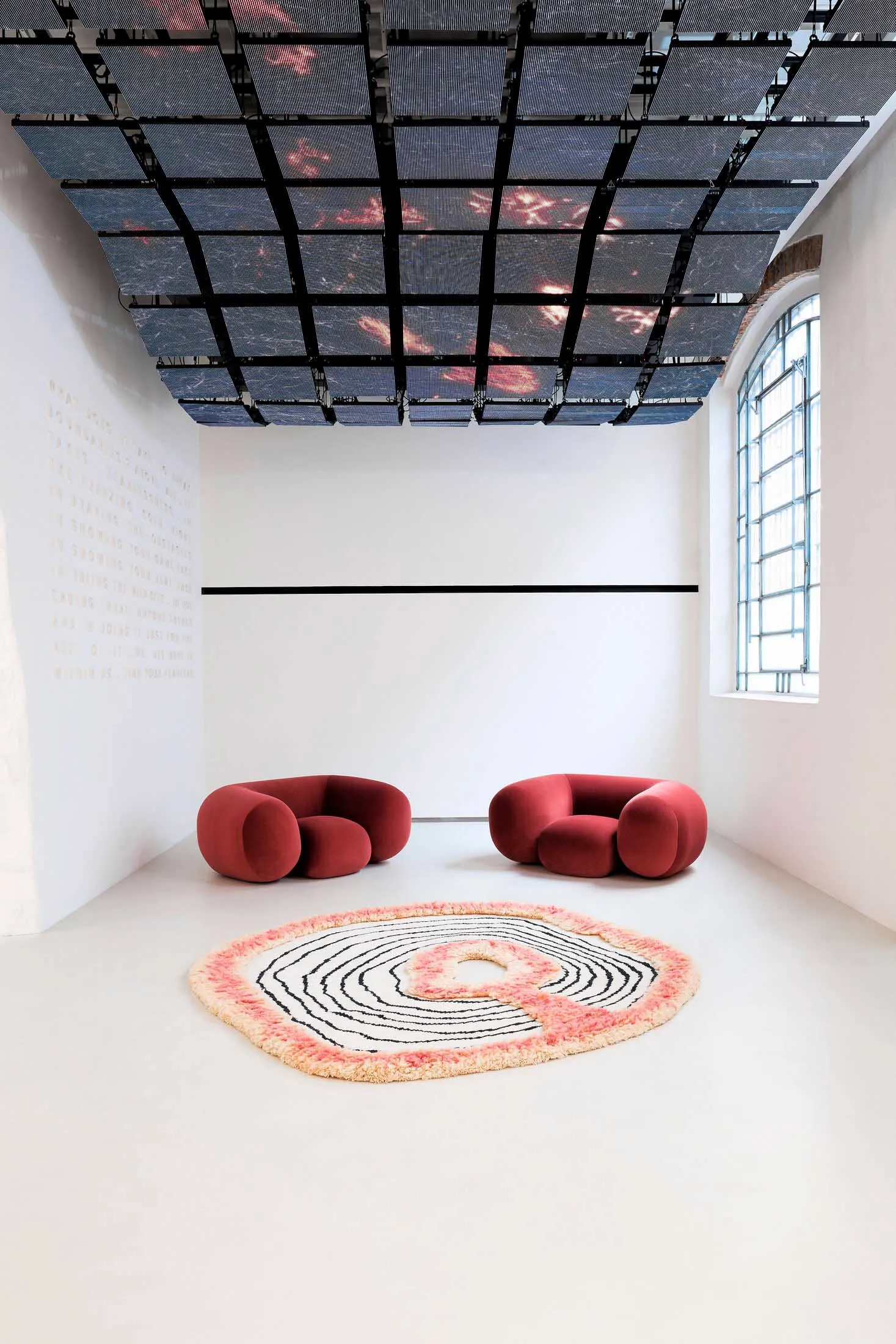 A minimalist interior design featuring two red sofas and a circular rug with concentric circles.