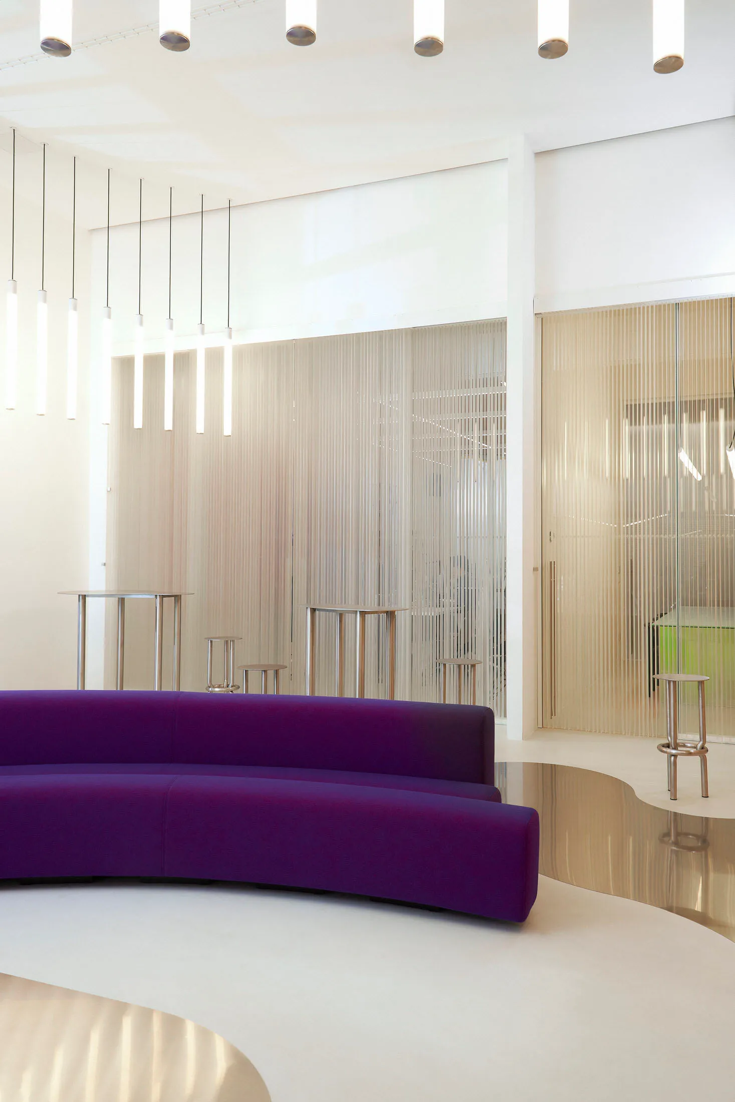 A minimalist office space featuring transparent glass panels, sleek white furniture, and modern lighting fixtures.