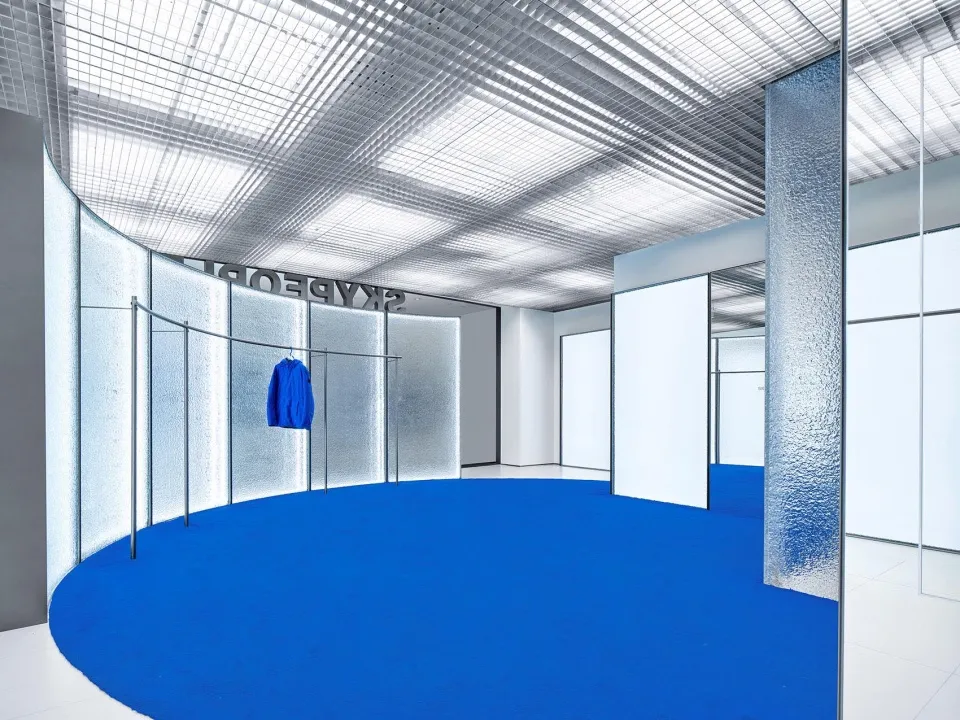 Modern minimalist retail store interior with glass walls, metal elements, and a blue rug on the floor.