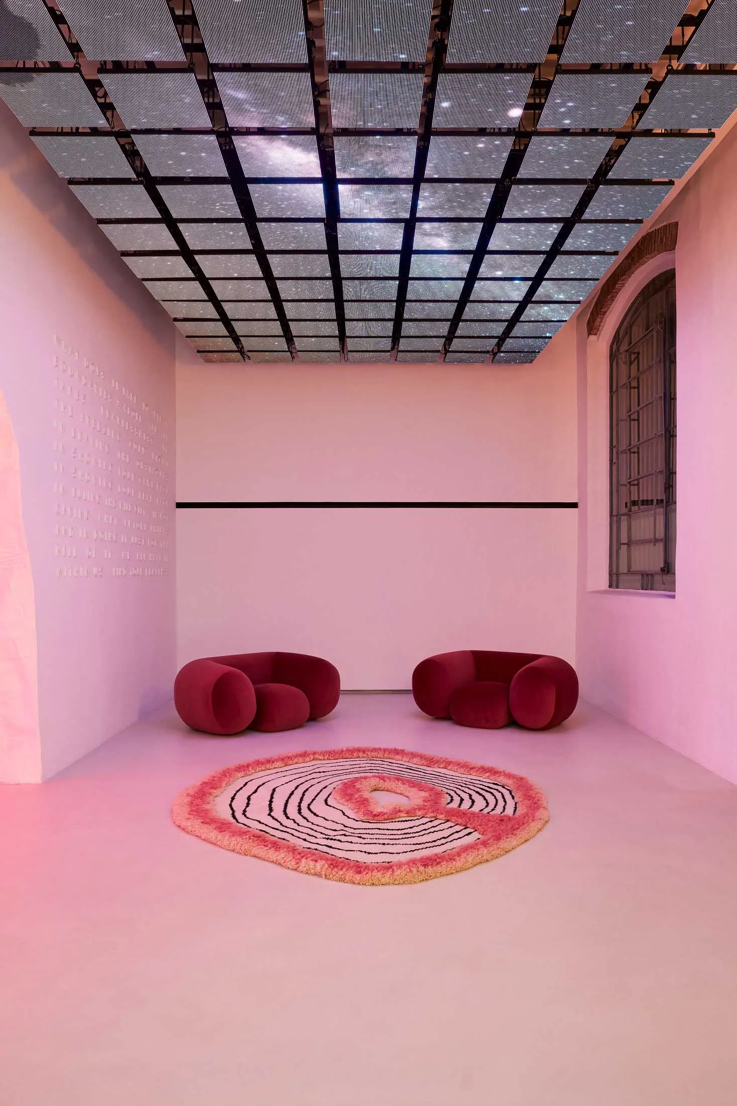 Minimalist interior design featuring soft, round seating furniture arranged in a circular pattern on a pink floor with a circ