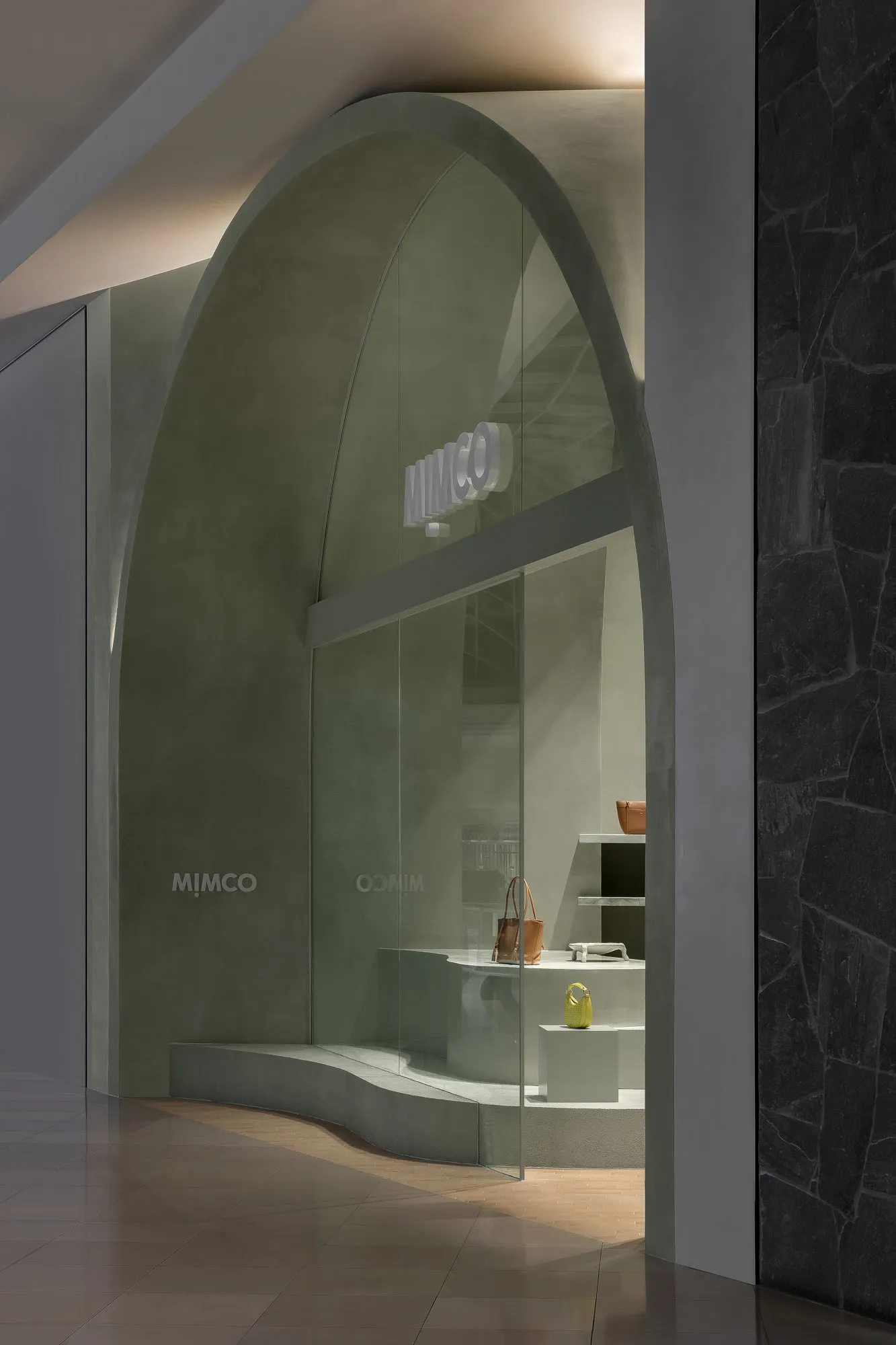 Modern, minimalist storefront with an arched, concrete entrance and a glass window displaying bags.